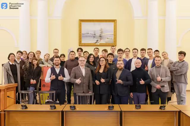 Спикер конференции в Томске на сцене с презентацией и светом репортажной съёмки.